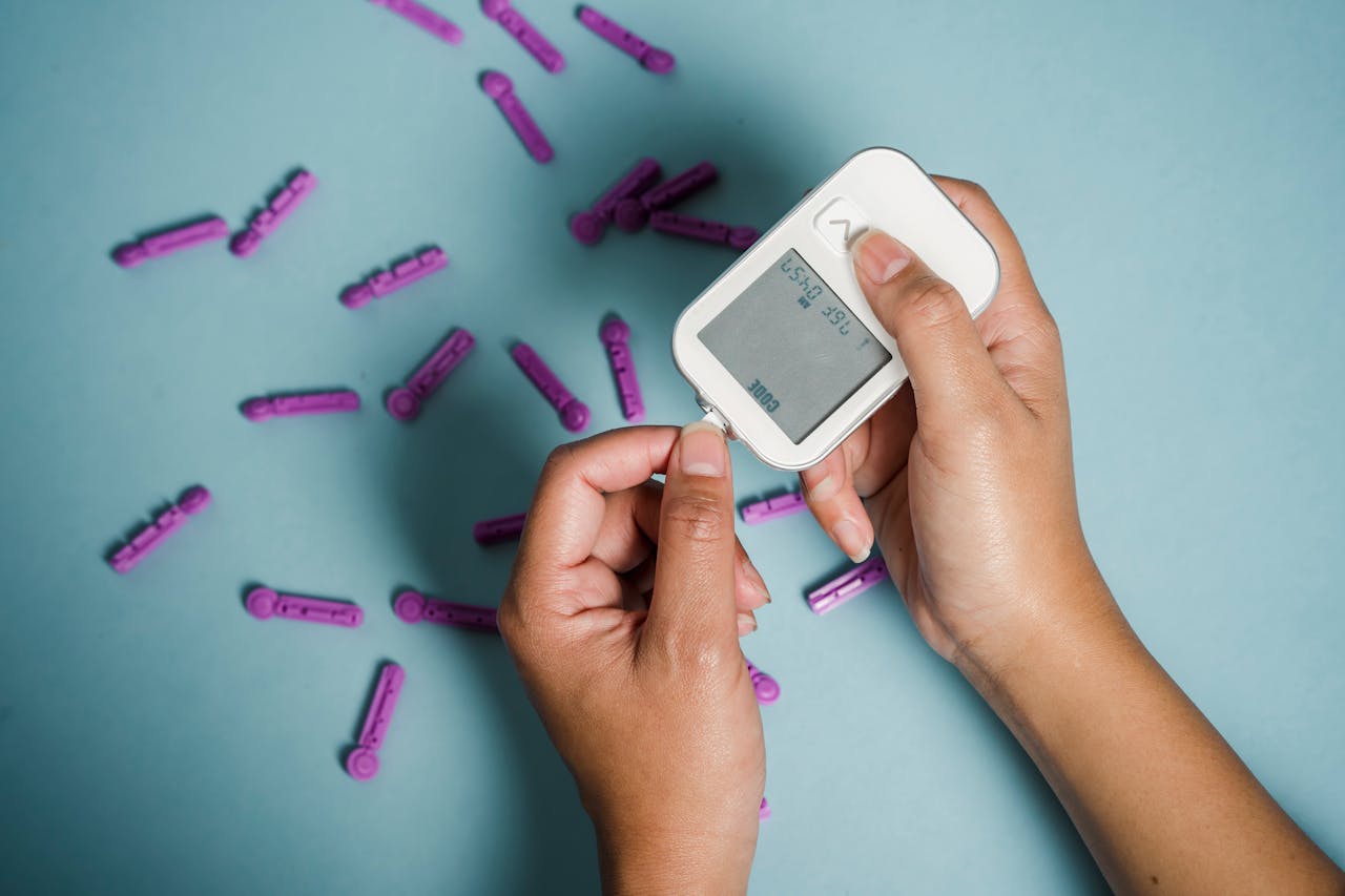 Top view of crop anonymous female diabetic measuring blood sugar with glucometer over scattered lancets